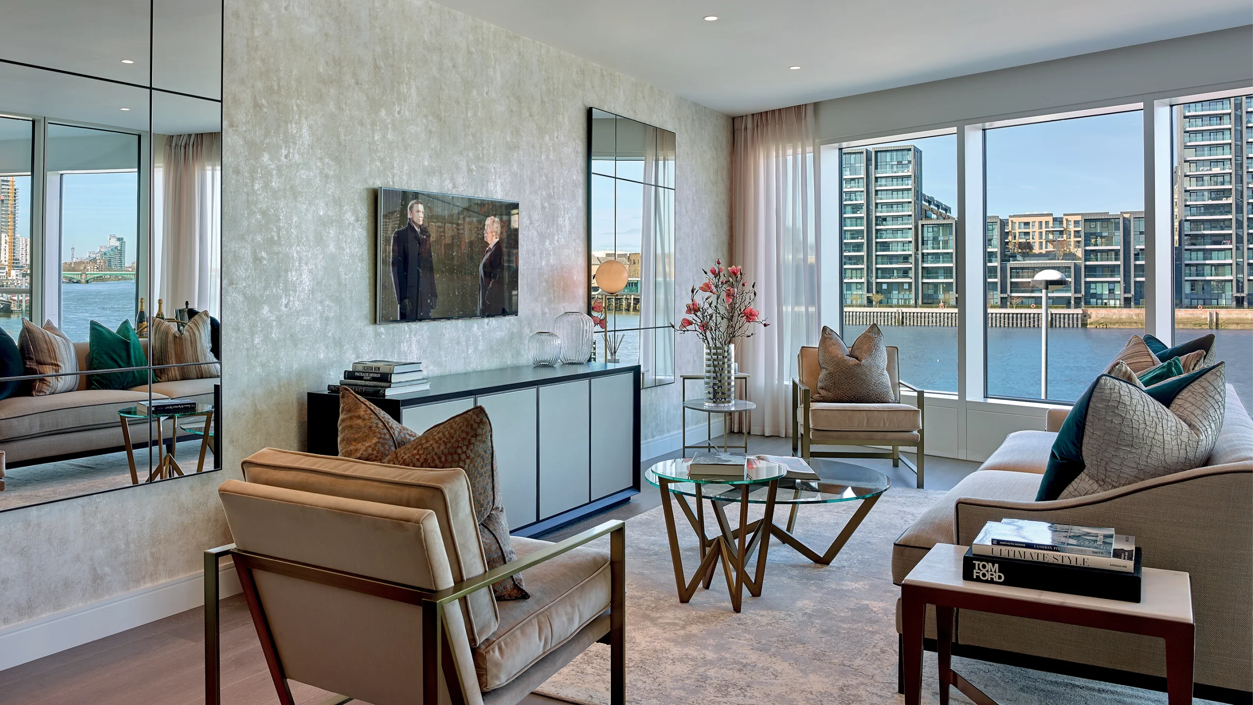 living room fitted with rugs, two armchairs, a sofa, two coffee tables, cabinet, television and two mirrors. Tall windows look out onto the River Thames